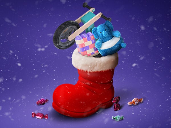 Ünnepi karácsonyi jelenet, amelyben egy nagy, fehér szegélyű piros csizma van, tele ajándékokkal, lila havas háttér előtt. A csizmában egy kis fa futóbicikli, egy kék plüss elefánt és egy színes építőkocka készlet látható. A csizma körül színes, csomagolt cukorkák hevernek a havas felületen. A levegőben hópelyhek hullanak.